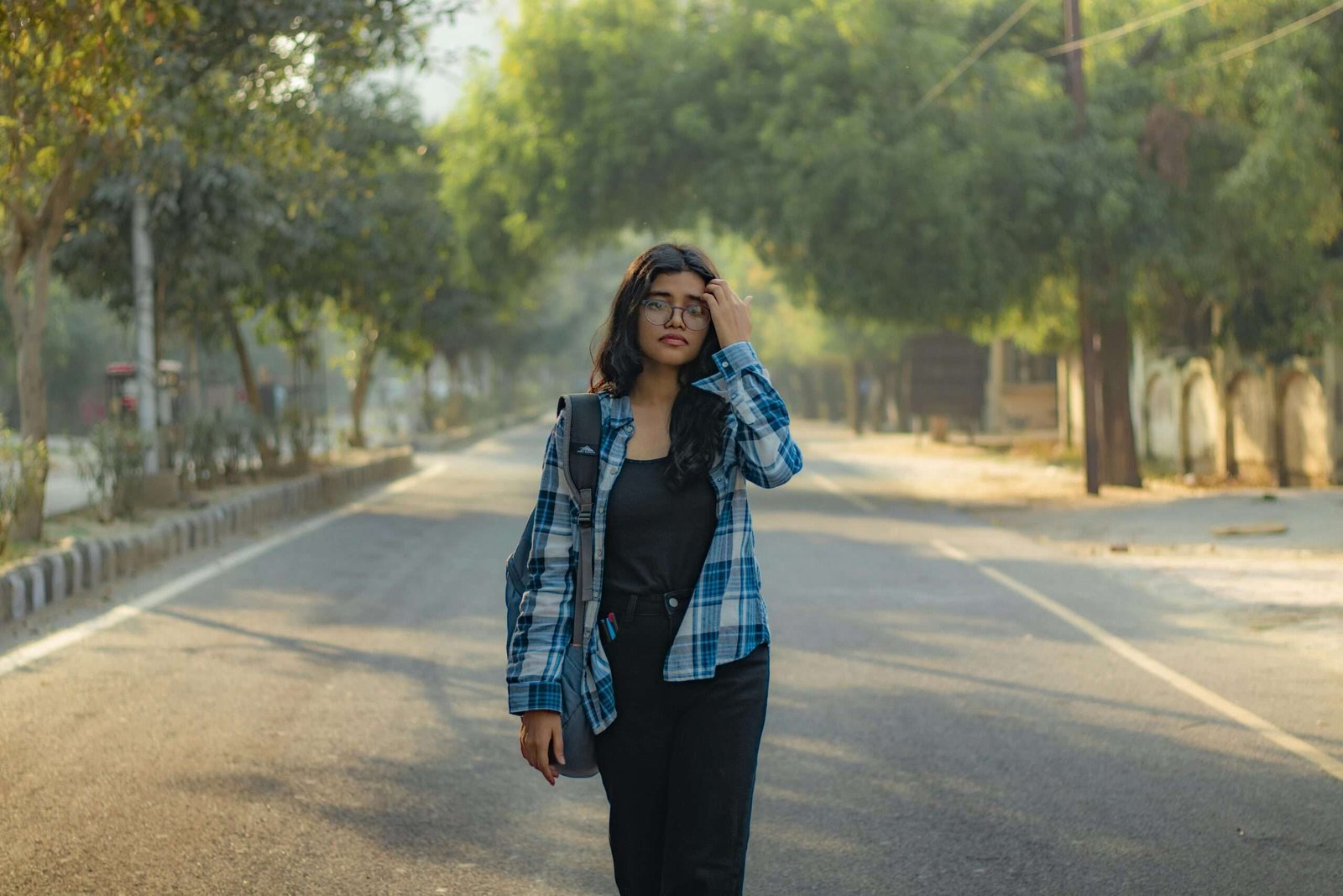 Young woman in casual attire walking down a tree-lined street, showcasing urban lifestyle and fashion.
